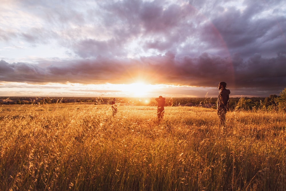 three person standing on brown grass under white clouds during sunset