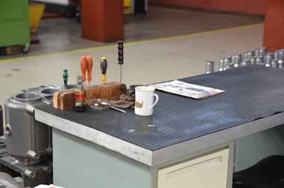 A sleek industrial drill resting on a steel workbench with blueprints in the background.