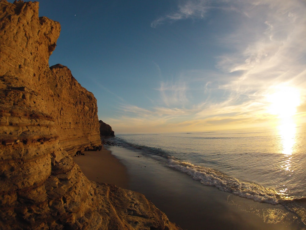 A tall rock wall behind a small beach area, taken during sunset.