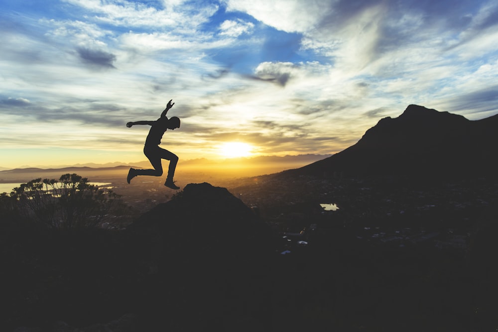 person jumping on hill during sunset