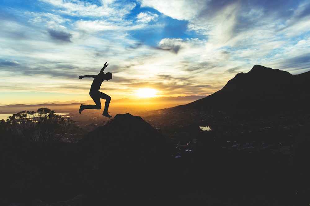 Silhouette of a man jumping high above a hilltop against a beautiful sky at sunset