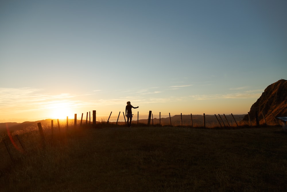 silhueta do homem em pé no meio do campo de frente para o pôr do sol