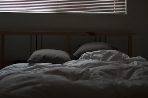 Lit défait dans une chambre sombre, éclairée par la lumière d’une fenêtre