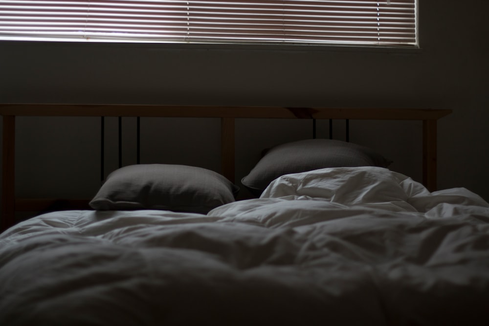 Ruffled gray covers and sheets with two pillows and a large window with blinds above it