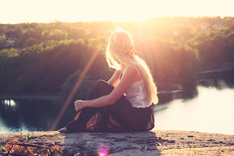 woman sitting on brown surface watching at body of water
