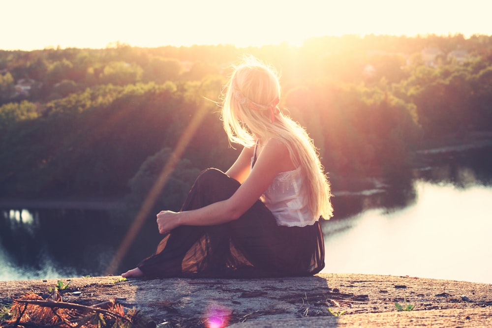 woman sitting on brown surface watching at body of water