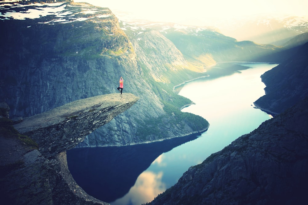 person standing on rock ledge doing yoga pose