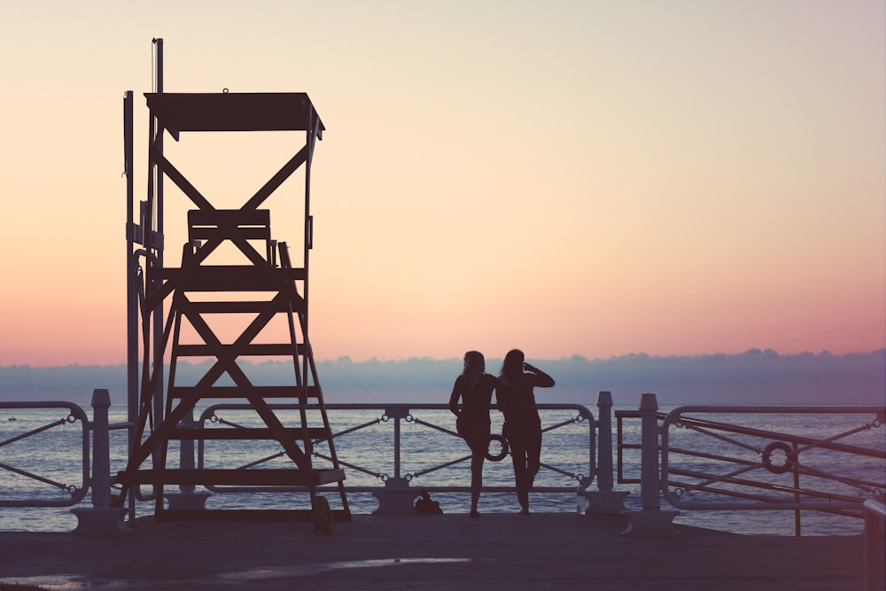 silhouette of two woman beside lifeguard tower