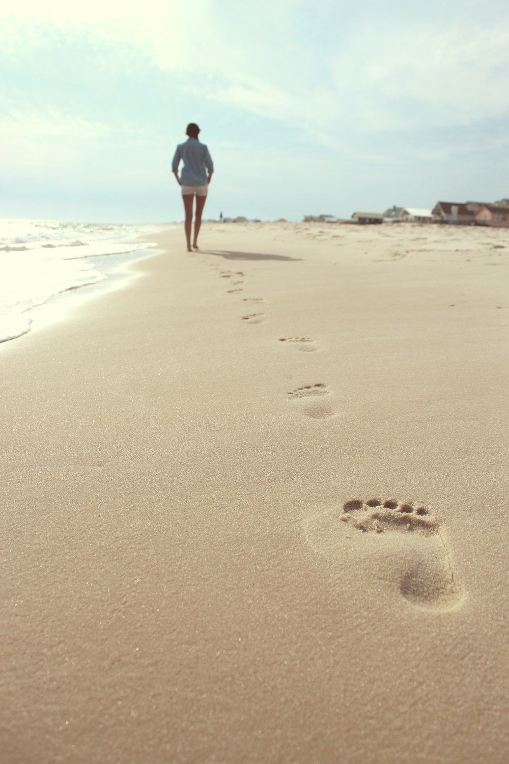 파란 드레스 셔츠와 흰색 짧은 반바지를 입고 해변을 걷는 여자