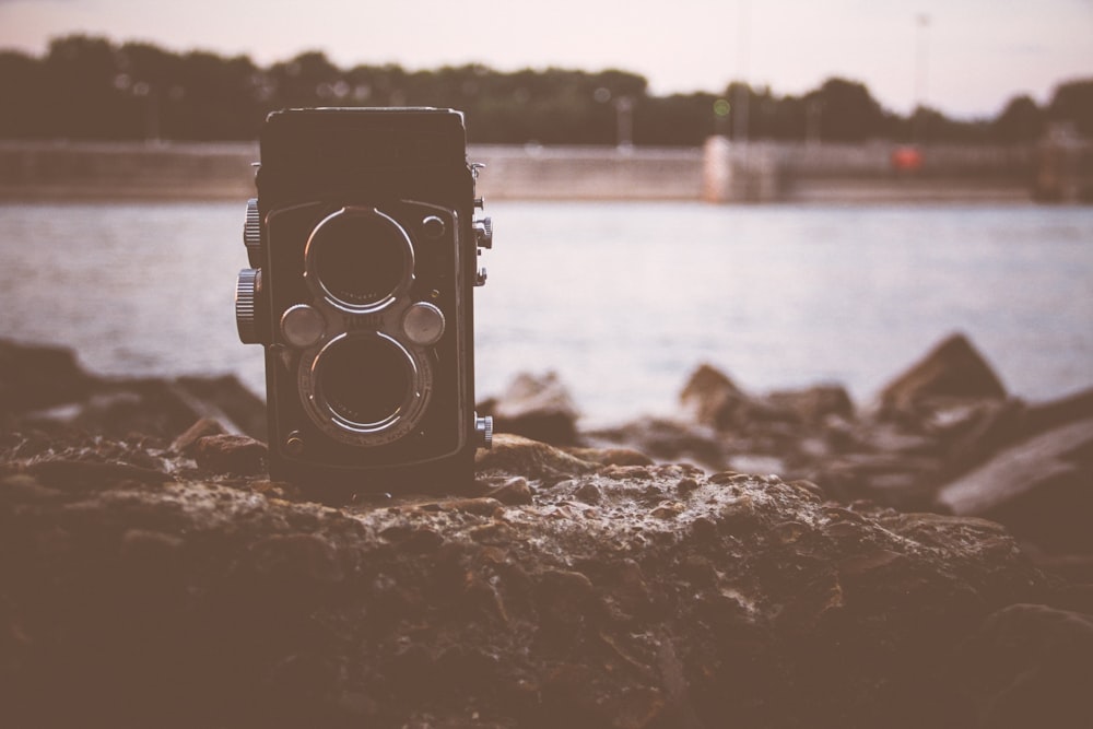 black land camera on rock in front of body of water during daytime