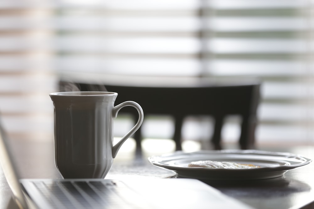 white ceramic mug beside plate on table