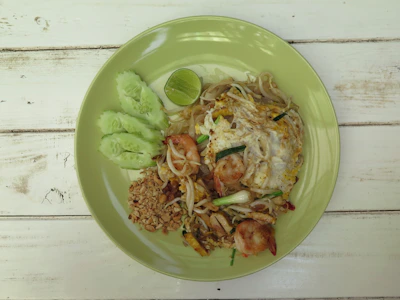 Vibrant pad thai plated with fresh herbs, illuminated by elegant golden accents.