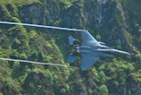 Advanced fighter jet soaring above mountainous terrain at dawn.