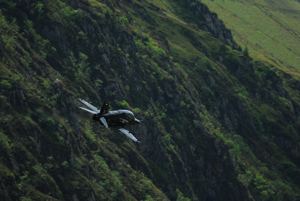 black airliner in flight above green mountains