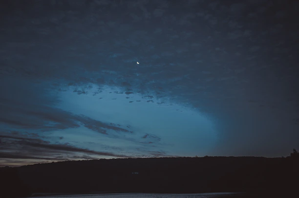 A serene night sky with subtle stars and a crescent moon casting gentle light over a quiet landscape.