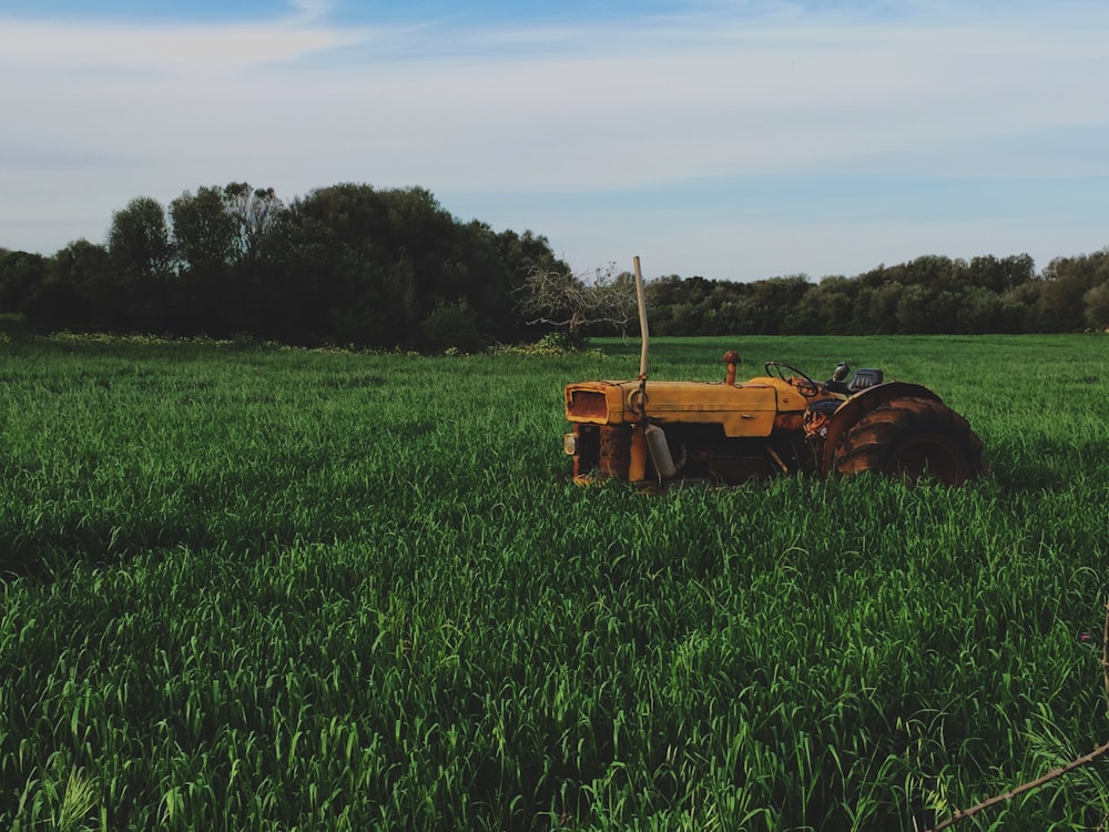 yellow farm tractor on green grassfield