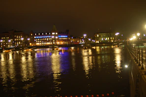 An evening cityscape with glowing windows and a calm river reflecting the lights
