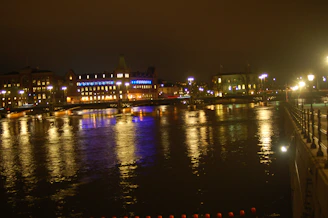 An evening cityscape with glowing windows and a calm river reflecting the lights