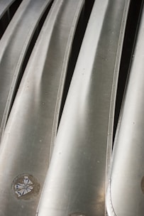 A close-up view of several metallic structures aligned in parallel, with a smooth and shiny surface. There are visible bolts or rivets along the edges of the metallic panels, and the surface reflects light at various angles.