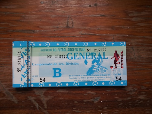 A vintage ticket for an Argentine football match, with blue and white colors. The ticket features text indicating 'Asociación del Futbol Argentino' along with 'Campeonato de 1ra. División'. There is an image of a football player on the right side. The ticket includes numbering and series information.
