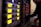 A series of electronic audio devices with illuminated yellow LED screens and small control knobs. The equipment is stacked in a rack format, and a person is visible in the background, slightly blurred, likely operating the gear.