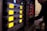 A series of electronic audio devices with illuminated yellow LED screens and small control knobs. The equipment is stacked in a rack format, and a person is visible in the background, slightly blurred, likely operating the gear.