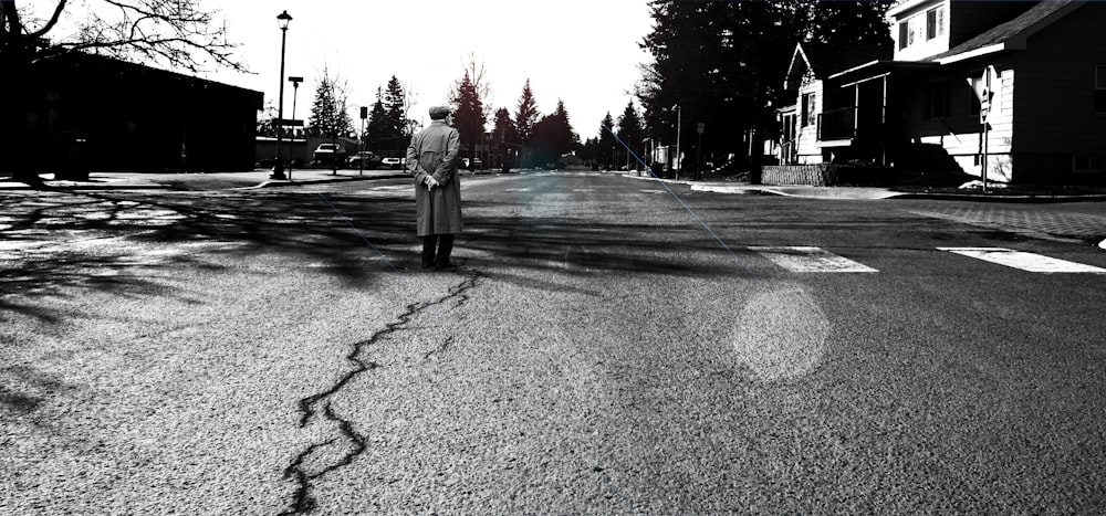 man standing in the middle of the road grayscale photography