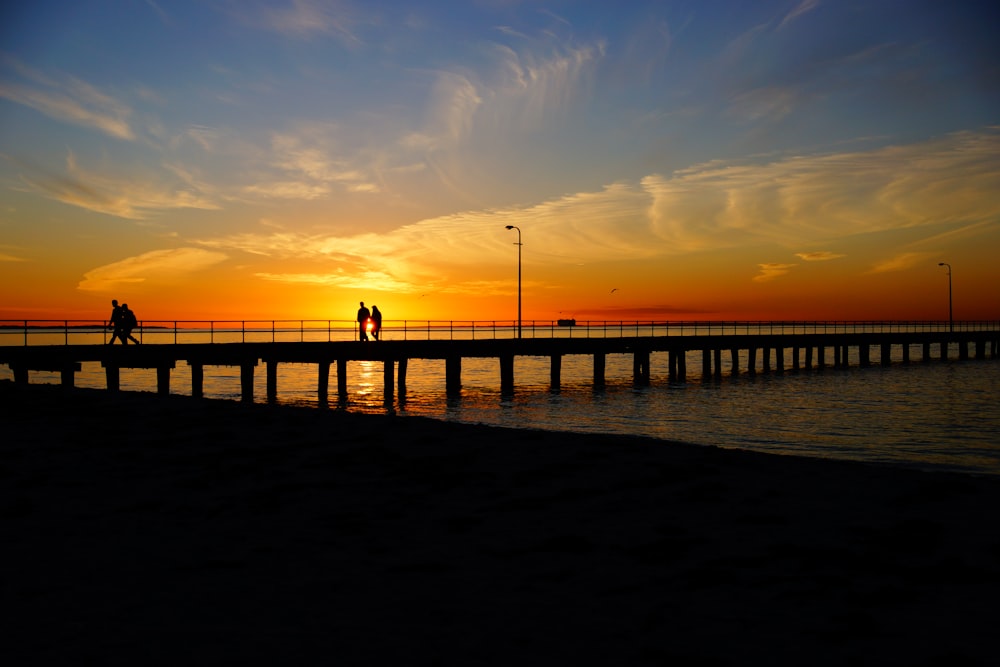 silhouette of people walking on bridge