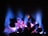 Vivid blue flames ascend from a collection of glowing coals, casting a warm, inviting glow. The colors transition from deep blue at the tips to a vibrant pink near the base, illuminating the textured surfaces of the coals.
