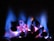 Vivid blue flames ascend from a collection of glowing coals, casting a warm, inviting glow. The colors transition from deep blue at the tips to a vibrant pink near the base, illuminating the textured surfaces of the coals.