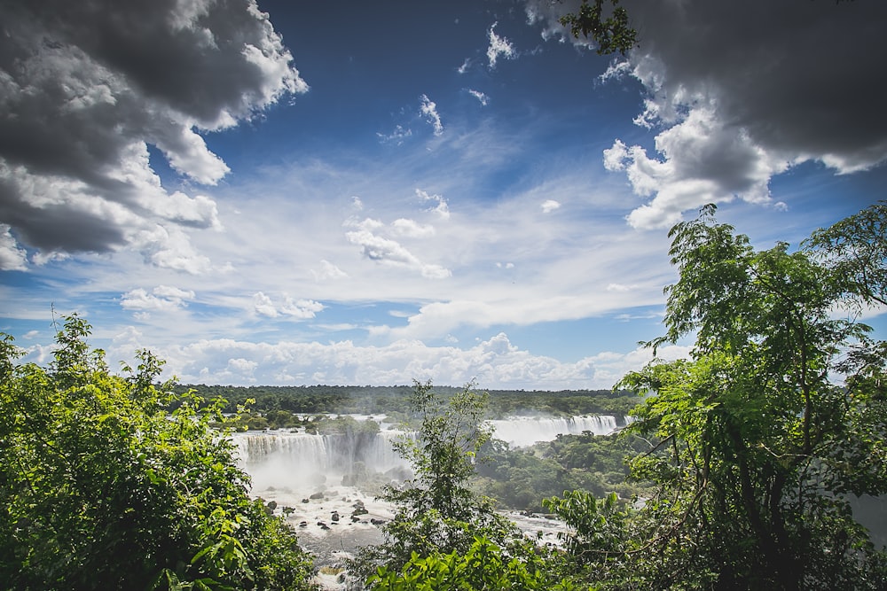 waterfalls surrounded by trees under cloudy sky