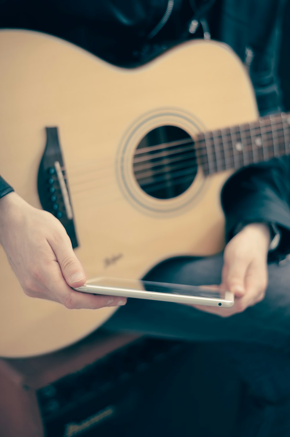 person with guitar on lap holding tablet