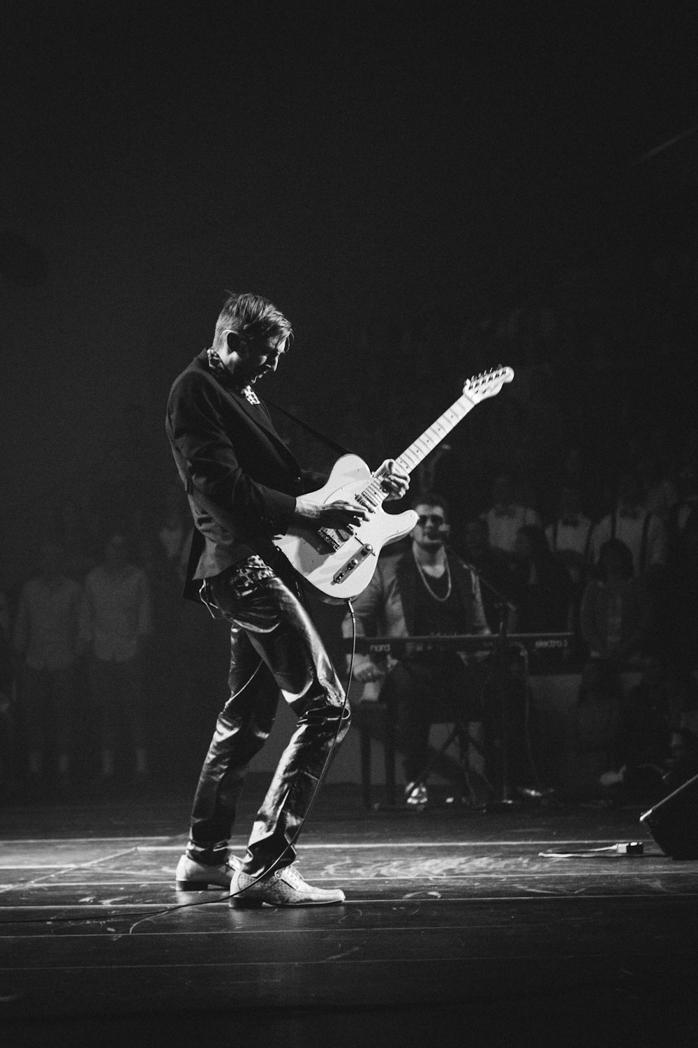 fotografia em tons de cinza do homem tocando guitarra elétrica perto do homem tocando teclado elétrico