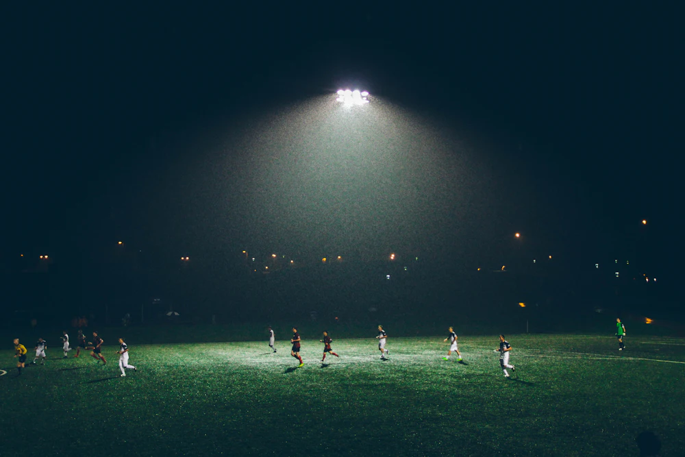 A floodlit pitch at night, players small under the lights