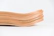 A stack of skateboard decks is displayed, showcasing multiple layers of wood with alternating red and natural tones. The decks are arranged in a slightly concave shape, which is typical for skateboard construction.