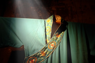 Close-up of delicate embroidery on a deep forest green cloak, lit by soft candlelight.