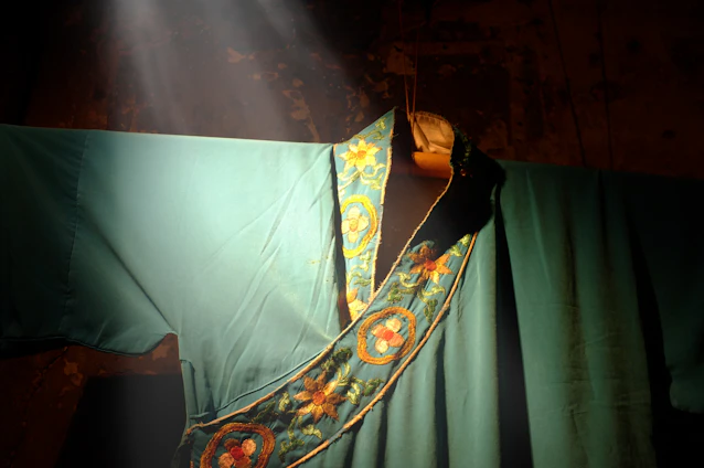 A close-up of a luxurious Moroccan thobe showcasing gold embroidery and turquoise accents under soft, dramatic lighting.