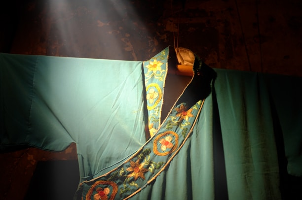 Close-up of delicate embroidery on a deep forest green cloak, lit by soft candlelight.