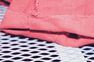 Close-up of a pink fabric with stitching detail, resting on a white perforated surface that creates a grid pattern.