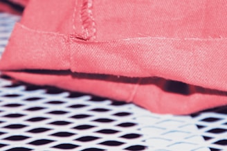 Close-up of a pink fabric with stitching detail, resting on a white perforated surface that creates a grid pattern.