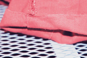 Close-up of breathable fabric texture with subtle electric coral stitching.