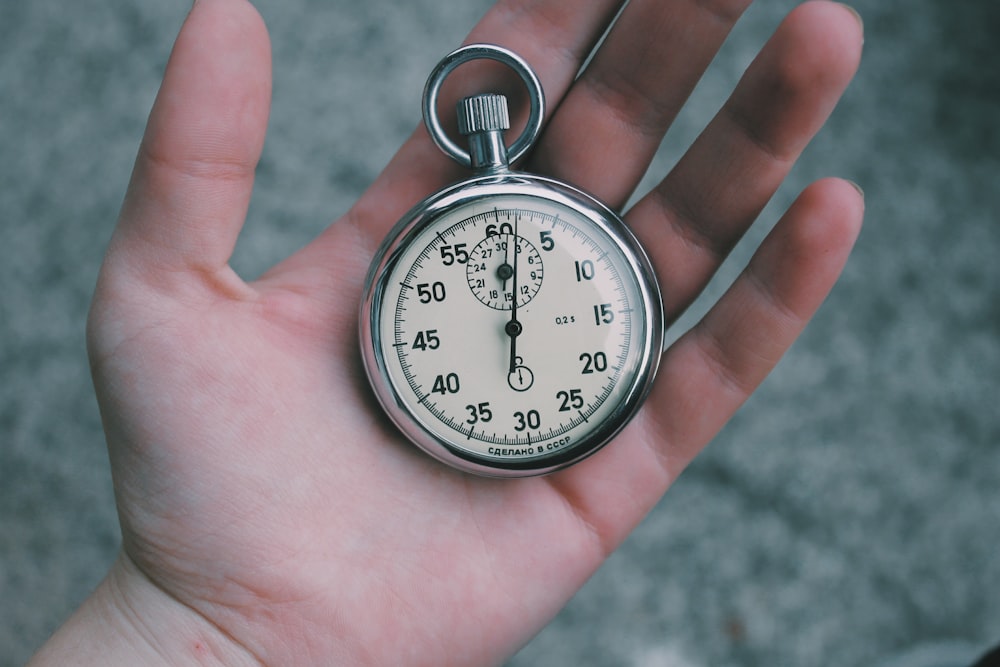 Persona que sostiene un reloj de bolsillo de color blanco y plateado