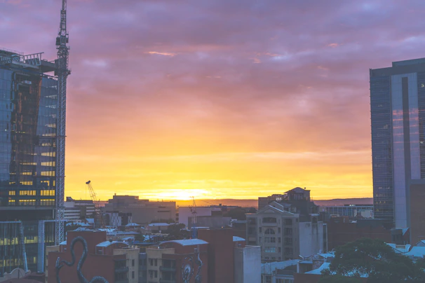 A panoramic view of a modern construction site with cranes and workers assembling a high-rise building at sunset.