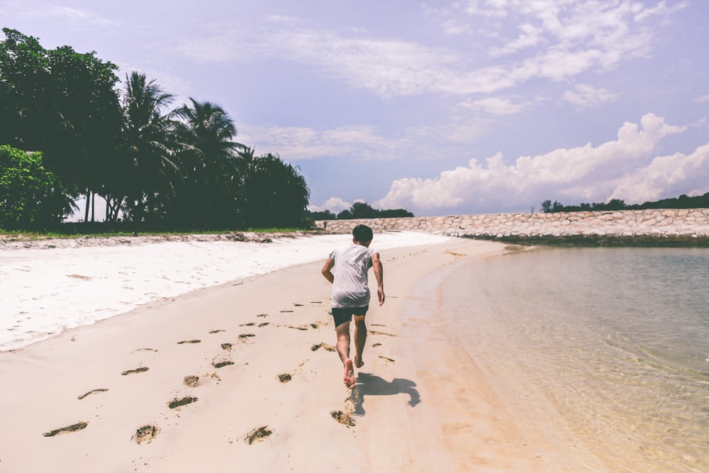 man wearing white t-shirt running in the sand