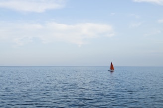 A sleek red sailboat cutting through calm blue waters under a clear sky