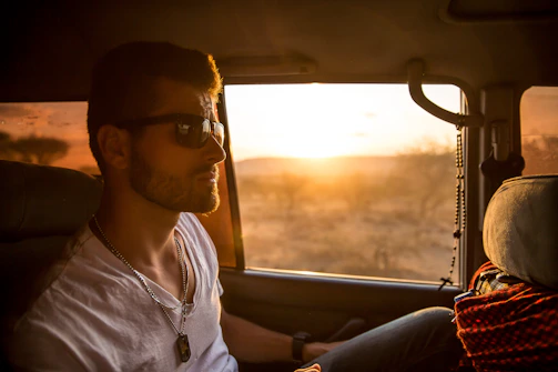 A friendly local driver smiling beside a car with a Zanzibar sunset in the background.