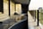 A modern balcony or corridor area with a curved granite handrail and glass panels supported by metal fixtures. The warm light casts subtle shadows and reflections on the granite surface and walls, creating a serene and minimalistic architectural space.