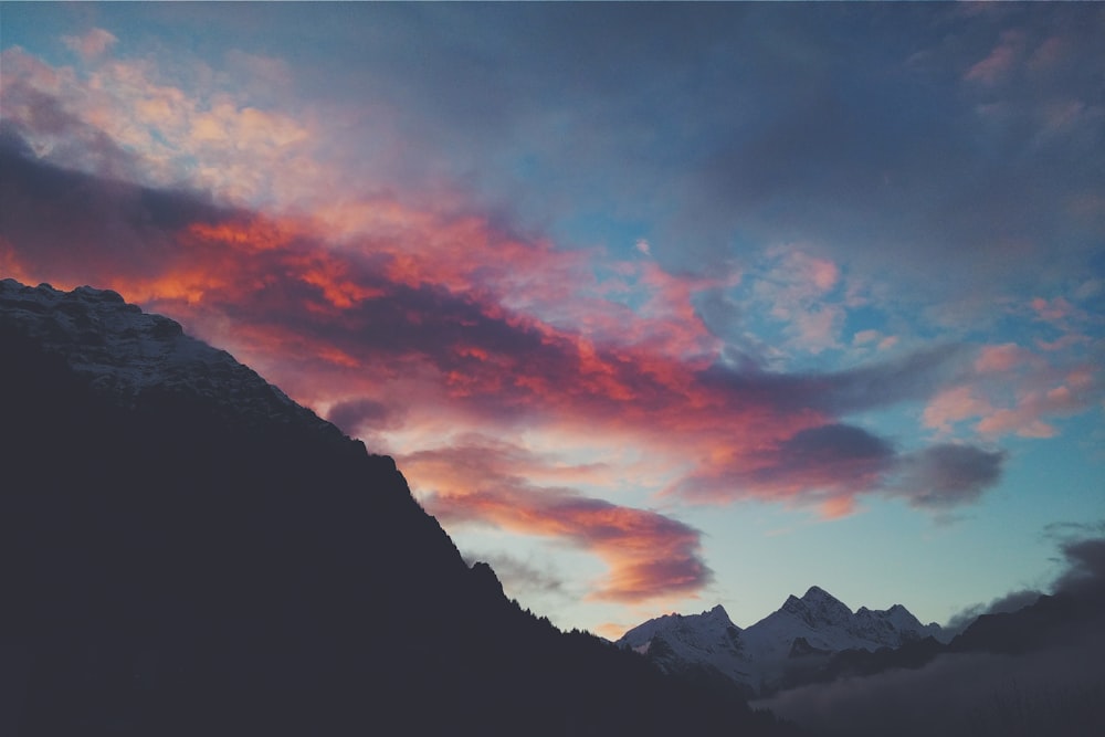 montanha coberta de neve sob nuvens vermelhas e céu azul