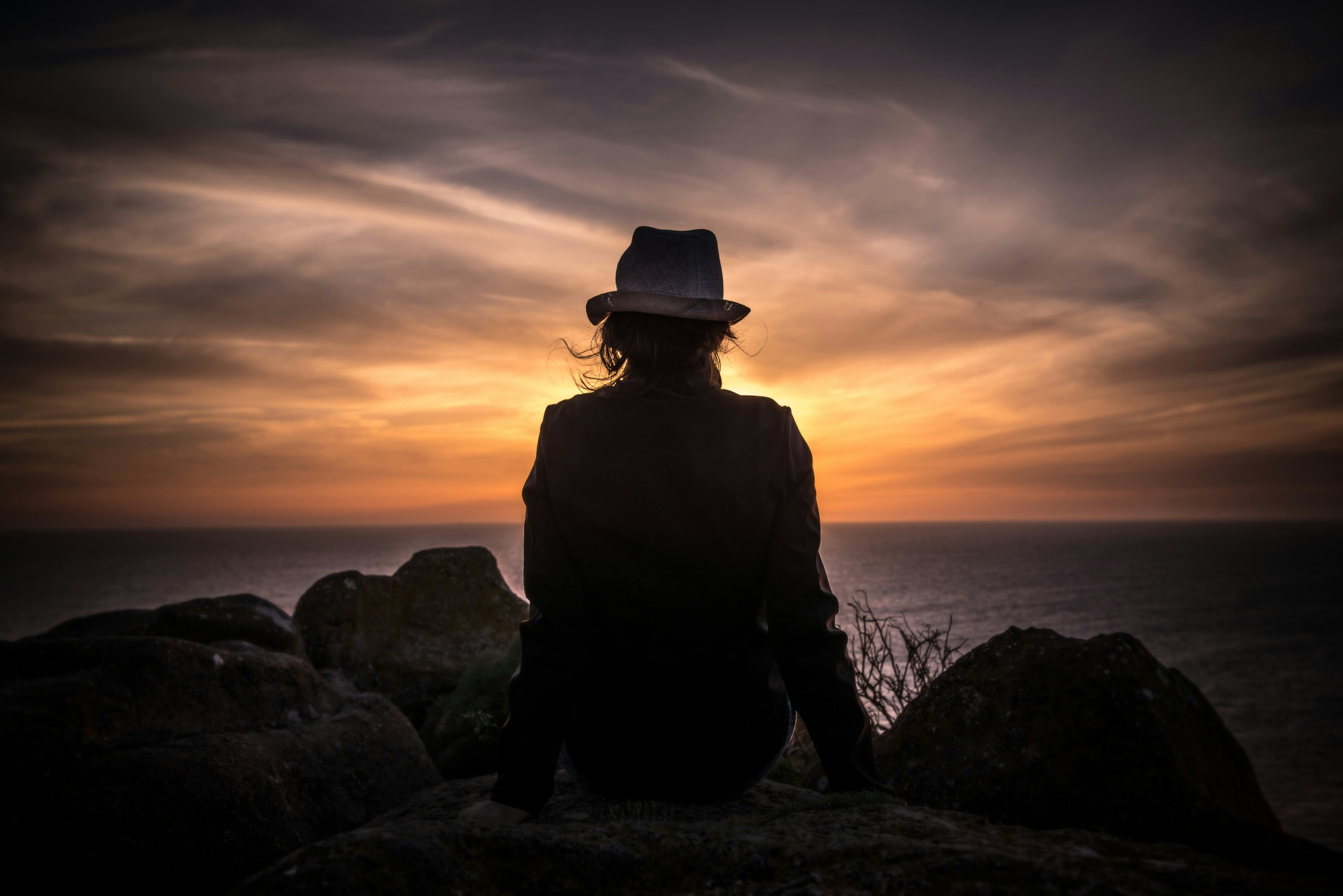 silhouette of man sitting on stone looking at body of water