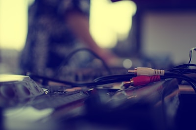 A close-up view of audio equipment with audio cables, featuring red and white connectors, laying on the surface. The background is blurred, suggesting a focus on the cables and a soft depth of field.